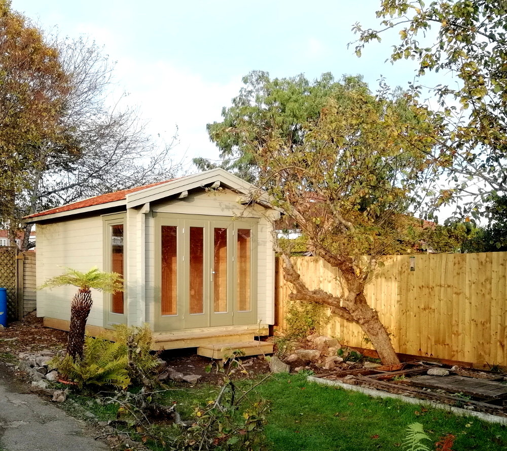 Traditional garden log cabin with glazing to the front face.  Pitch roof, used as a garden office. Gallery Image