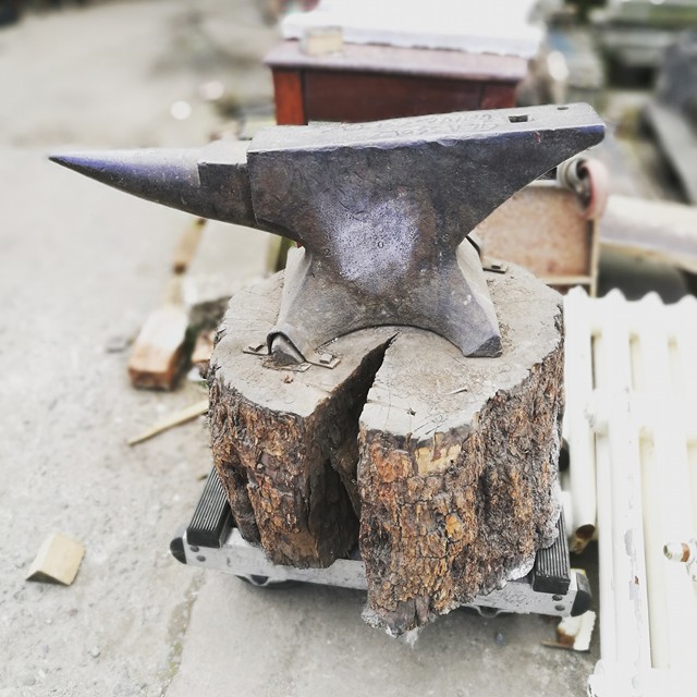 Anvil mounted on great bit of rough cut timber. Gallery Image
